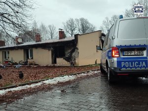 Fragment radiowozu i budynek, w którym wybuchł pożar.