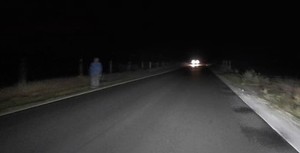 Mężczyzna idący w nocy poboczem jezdni.