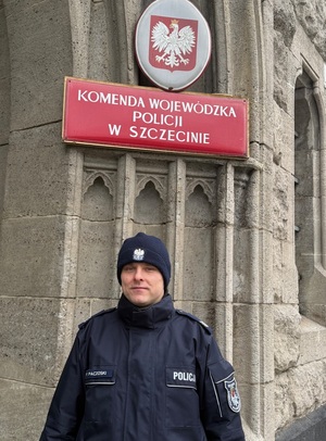 Umundurowany policjant pod tablicą : komenda Wojewódzka Policji w Szczecinie.