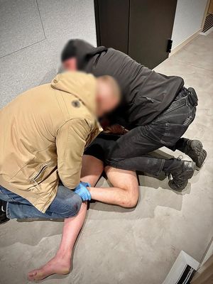 Dwaj funkcjonariusze zakładają kajdanki mężczyźnie lezącemu na ziemi.