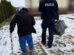 senior idzie o lasce, obok idzie policjant.