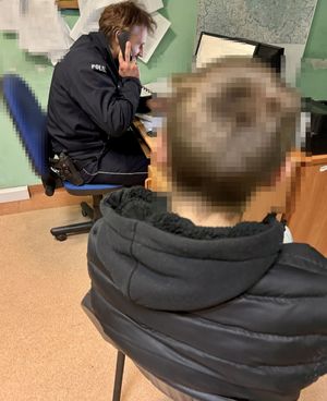 Policjant siedzi przy biurku i rozmawia przez telefon. Z tyłu widać zatrzymanego.