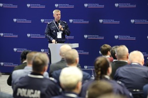 Uczestnicy konferencji na sali w MSWiA słuchają policjanta przemawiającego do nich stojąc przy mównicy.