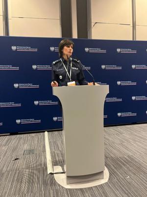 Policjantka stoi przy mównicy przemawiając do zgromadzonych na sali.