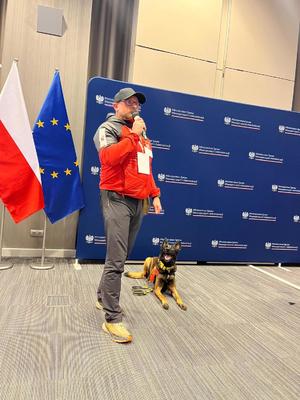 Mężczyzna z psem na smyczy podczas wystąpienia na konferencji.