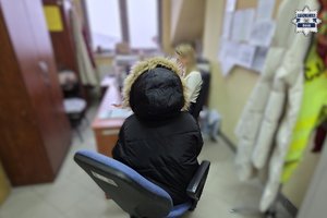 Odwrócona tyłem kobieta siedzi na krześle w pomieszczeniu.