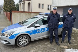 policjanci stoją obok radiowozu.