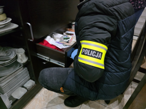 Policjant przeszukuje szuflady komody.