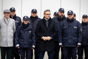 Umundurowani policjanci a wśród nich ubrany po cywilnemu mężczyzna.