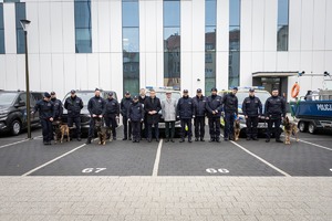 Zebrani goście na uroczystości, wśród nich przewodnicy z psami a za nimi policyjne furgony i łódź.