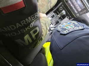 Fragmenty mundurów policjanta i żołnierza. Na mundurze policjanta naszywka z logo KPP w Piszu, a mundurze żołnierza napis: Żandarmeria Wojskowa MP.