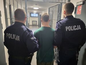 Dwaj funkcjonariusze trzymają zatrzymanego mężczyznę.