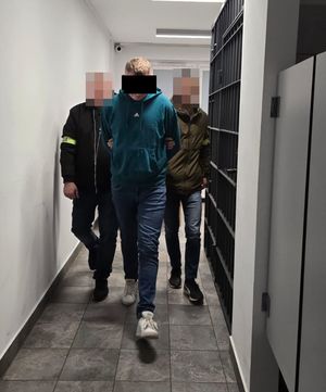 Dwaj policjanci prowadzą korytarzem zatrzymanego.