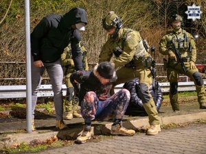 zdjęcie przedstawia funkcjonariuszy Policji oraz Straży Granicznej i mężczyznę, który siedzi na krawężniku.