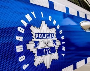 Policyjna odznaka na drzwiach bocznych radiowozu, a wokół niej napis: Pomagamy i chronimy.