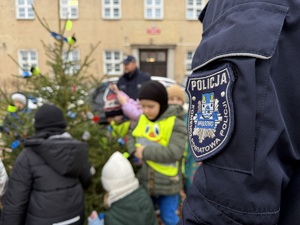 Dzieci i policjanci ubierają odblaskowa choinkę.
