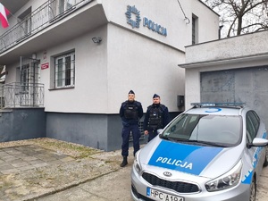 Policjanci przy radiowozie przed budynkiem Policji.