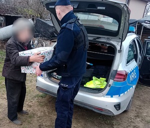Policjant wręcza paczki mężczyźnie. Obok widać policyjny radiowóz z otwartym bagażnikiem.