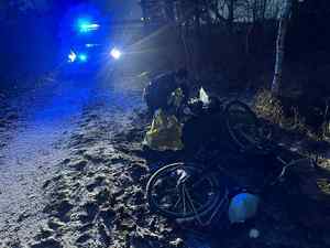 noc. policjant pomaga mężczyźnie leżącemu na chodniku, obok jest rower.