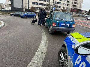 Funkcjonariusz pomaga mężczyźnie opuścić rondo przechodząc przed stojącym samochodem osobowym.