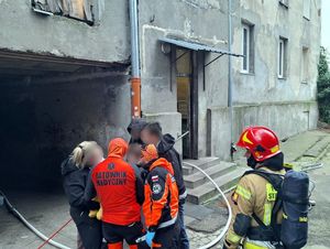 Policyjni wywiadowcy, ratownicy medyczni, strażak i uratowana kobieta z dziećmi przed budynkiem.