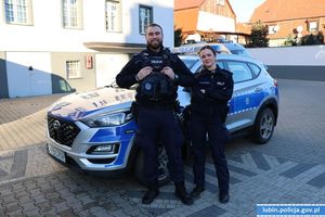 Policjant i policjantka stoją przy radiowozie.