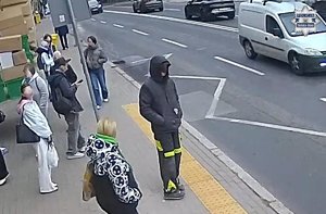 Stopklatka z nagrania monitoringu. Zatrzymany mężczyzna stoi na przystanku razem z innymi ludźmi.