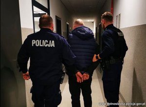 Policjanci prowadzą zatrzymanego korytarzem.