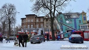 Pożar budynku, obok którego pracują służby m.in. Policji. Przy budynku wozy strażackie.