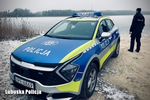 radiowóz nad wodą obok stoi policjant.