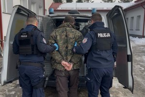 dwóch policjantów prowadzi do radiowozu zatrzymanego.