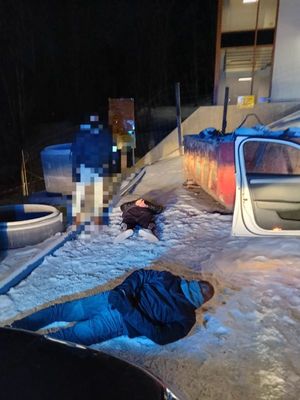 Dwaj zatrzymani mężczyźni leżą na śniegu zakuci w kajdanki. Obok nich stoi funkcjonariusz.