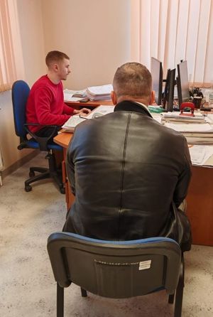 Zatrzymany mężczyzna siedzi na krześle. Przy biurku siedzi policjant, który go przesłuchuje.