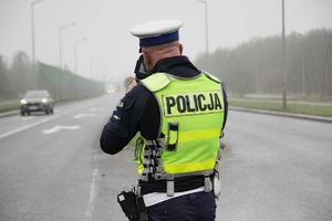Policjant ruchu drogowego sprawdza prędkość przejeżdżających pojazdów - widok z tyłu.