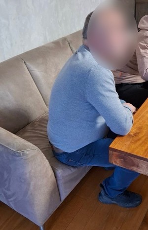 Zatrzymany siedzi na kanapie w mieszkaniu przy ławie.