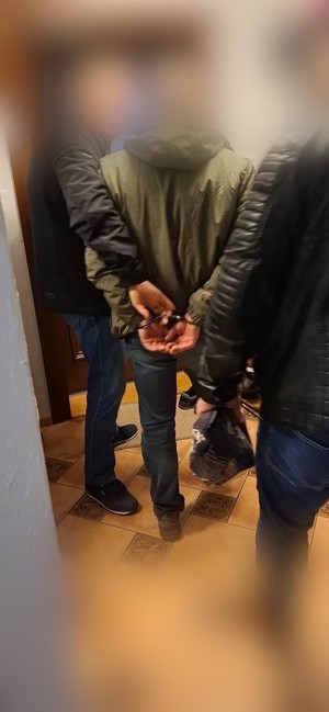 Dwaj funkcjonariusze  z zatrzymanym mężczyzną zakutym w kajdanki.