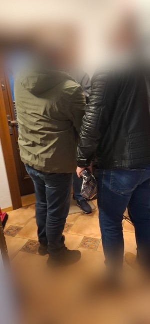 Dwaj funkcjonariusze  z zatrzymanym mężczyzną zakutym w kajdanki.