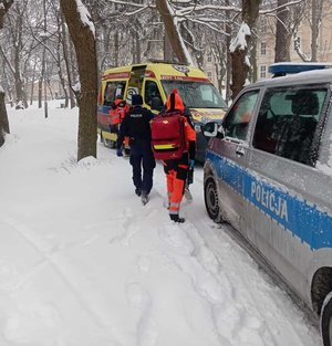 Dwaj ratownicy i policjant przy karetce pogotowia. Obok stoi radiowóz policyjny.