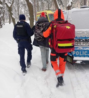 Policjant i ratownik prowadza mężczyznę do karetki.