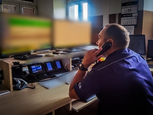 Policjant siedzący przy biurku przed monitorami rozmawia przez telefon stacjonarny.