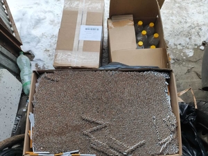 Zabezpieczone przez policjantów papierosy w kartonie, obok otwarty karton z butelkami z alkoholem.