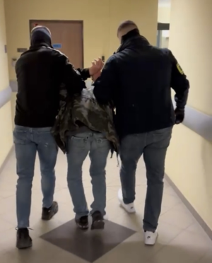 dwóch policjantów prowadzi zatrzymanego przez korytarz.