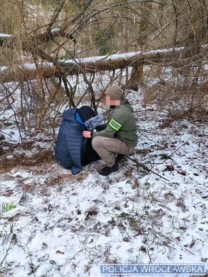 Policjant kuca przy odnalezionej kobiecie, która siedzi na ziemi.