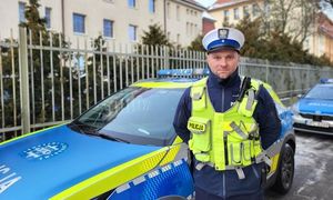 Policjant stoi na tle budynku obok radiowóz.