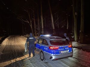 Dwaj policjanci przy radiowozie na leśnej,ośnieżonej drodze w lesie - pora nocna.