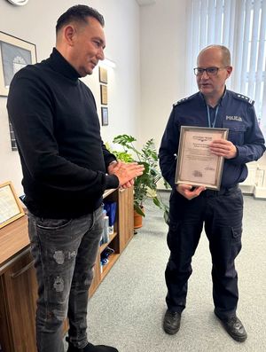 Mężczyzna w swetrze i policjant, który trzyma w ręku podziękowania.