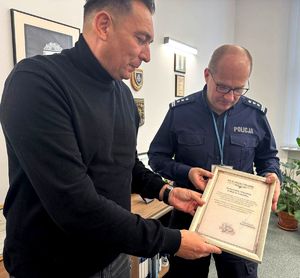 Mężczyzna w swetrze i policjant, który trzyma w ręku podziękowania.