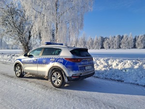 Radiowóz stoi na pokrytej śniegiem drodze. W tle pola pokryte śniegiem i drzewa.
