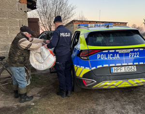 Policjant przy radiowozie daje mężczyźnie materac.