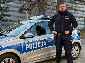 Policjant stoi przy radiowozie.